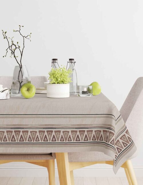 The image shows a table decorated with a patterned gray tablecloth, with flowers in a vase, bottles, and green apples.