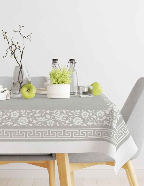 A table decorated with a patterned gray tablecloth, with flowers, green plants, bottles, and green apples.