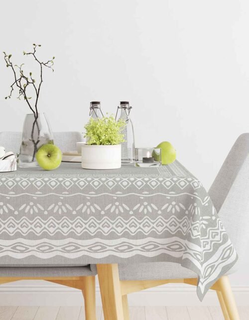 The image shows a table decorated with a patterned gray tablecloth, with flowers in a vase, bottles, a green apple, and a candle.