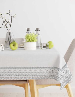 The table appears decorated with a white patterned tablecloth, with green flowers in a vase, bottles, and green apples.
